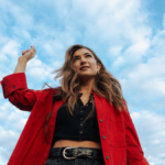 singer Tenille Townes, wearing a red coat, with blue sky behind