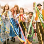 A group of three women and two men walking down a street carrying multi-coloured ribbons and streamers