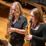Two girls dressed in black playing saxophones