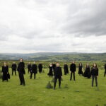 Members of Kantos Chamber Choir, dressed in black, in a field